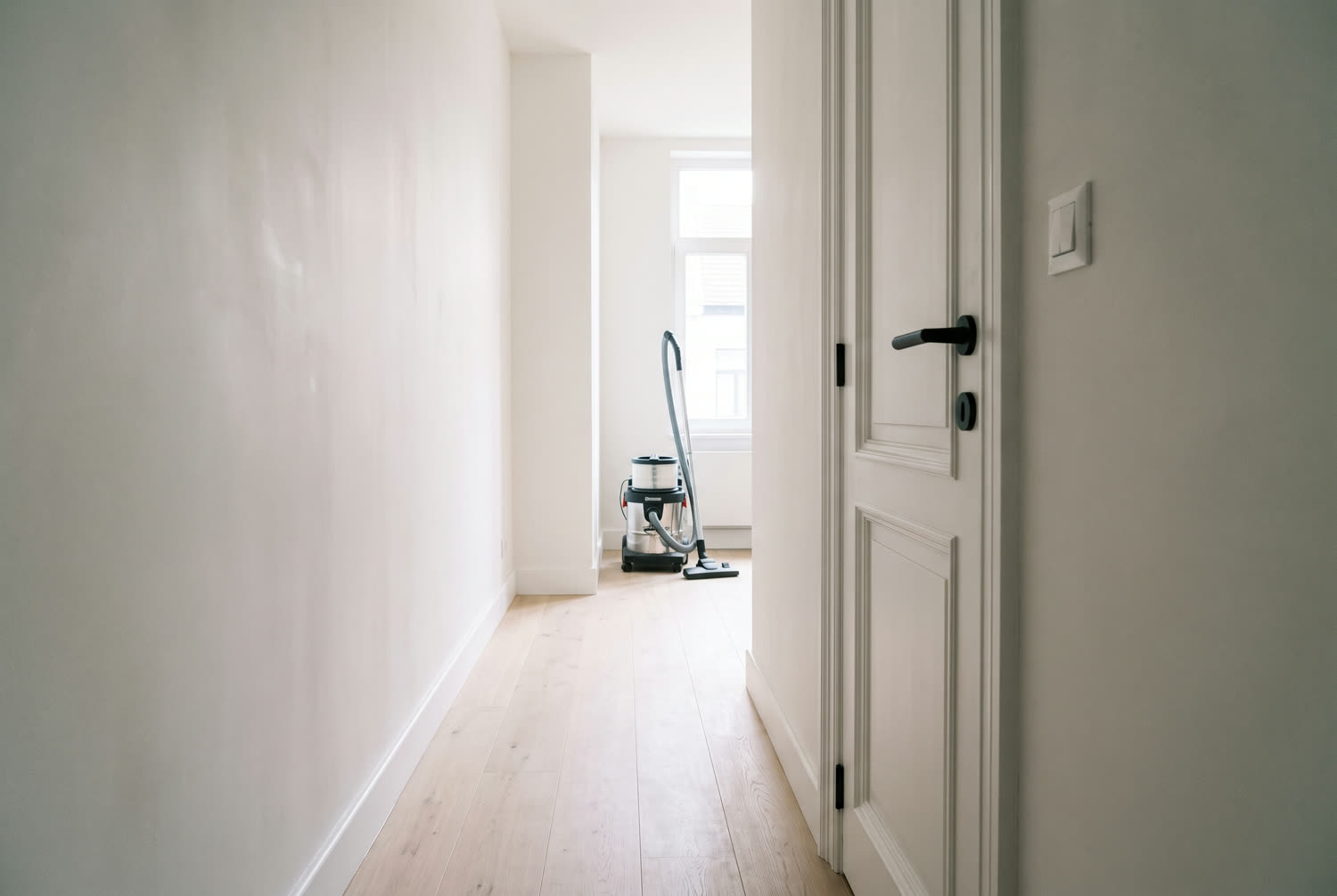 Couloir rénové en fin de chantier, enduit lisse, parquet chêne clair et aspirateur à filtre fin au fond
